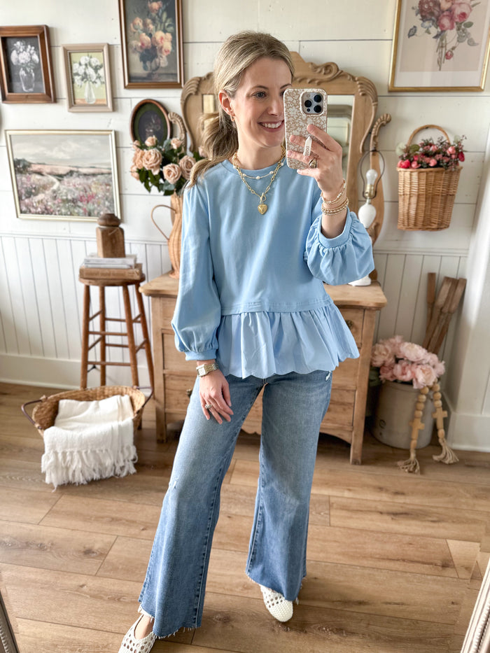 Woman taking a mirror selfie wearing a blue top and jeans in a home setting.