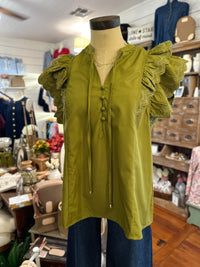 An olive green blouse with ruffled sleeves and a lace-up front, displayed on a mannequin torso in a clothing boutique.