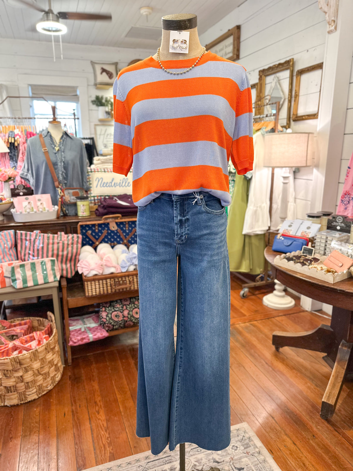 Mannequin wearing an orange and blue striped sweater and blue jeans in a store setting.