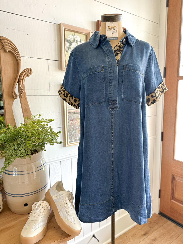 Blue denim dress with leopard print cuffs on a mannequin in a room with a plant and shoes.