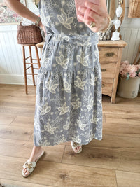 Person wearing a floral dress standing in a room with wooden flooring and furniture.