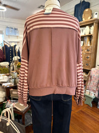 A dusty rose and brown striped long-sleeve sweatshirt with a solid dusty rose back panel, displayed on a mannequin wearing dark blue jeans inside a retail shop.
