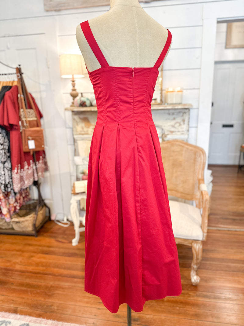Red dress on a mannequin in a store setting with wooden floor and clothing rack.