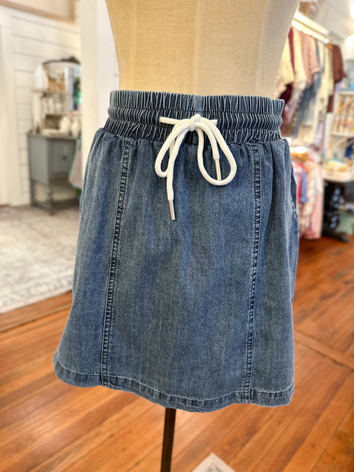 Blue denim skirt with a white drawstring on a mannequin in a store setting.