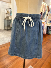 Blue denim skirt with a white drawstring on a mannequin in a store setting.
