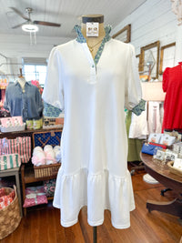 White dress on a mannequin in a store setting with various items in the background.