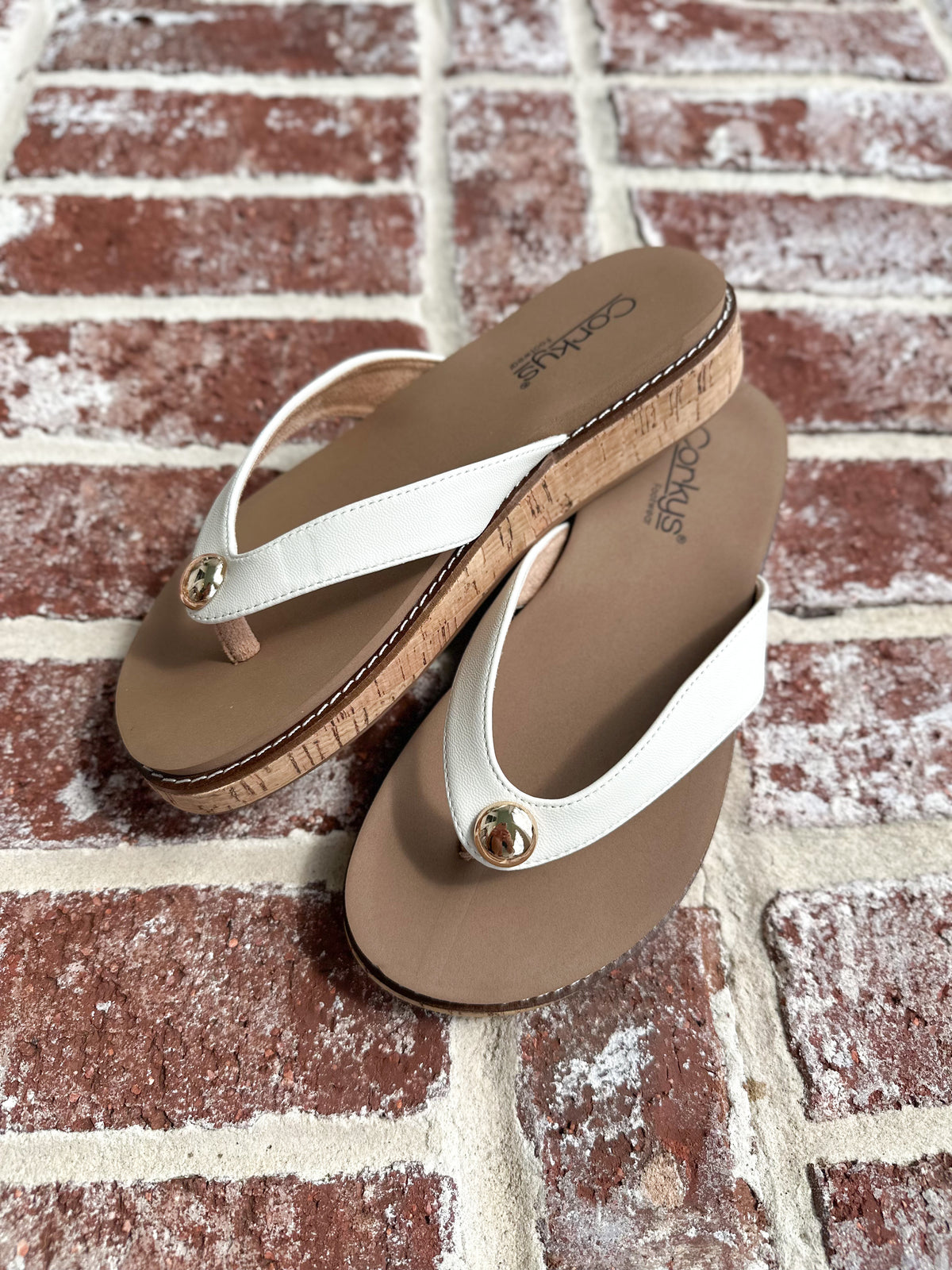 Pair of tan and white sandals on a brick surface