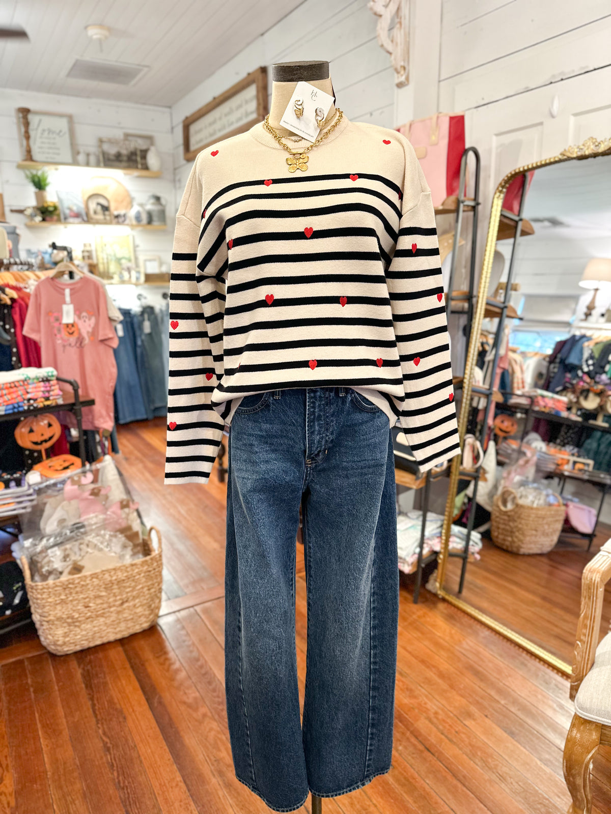 cream long sleeve sweater with black stripes and red hearts  with barrel jeans inside boutique store 