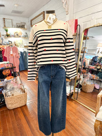 cream long sleeve sweater with black stripes and red hearts  with barrel jeans inside boutique store 