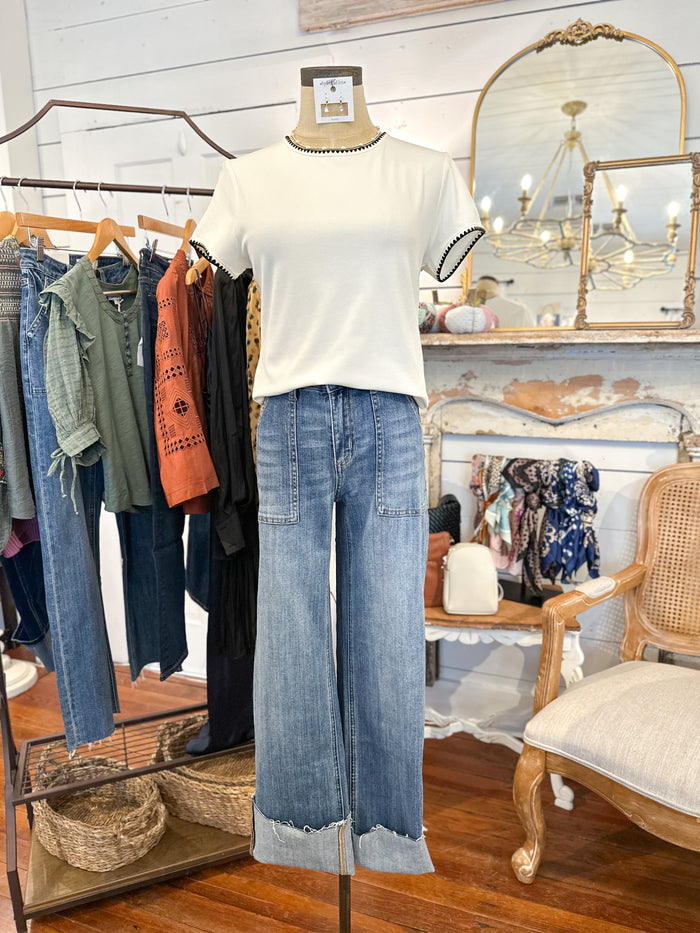 Mannequin wearing a white shirt and blue jeans in a clothing store setting with racks and mirrors.
