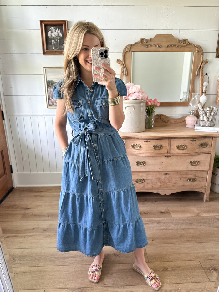 Woman taking a mirror selfie wearing a blue denim dress with pockets and adjustable belt 