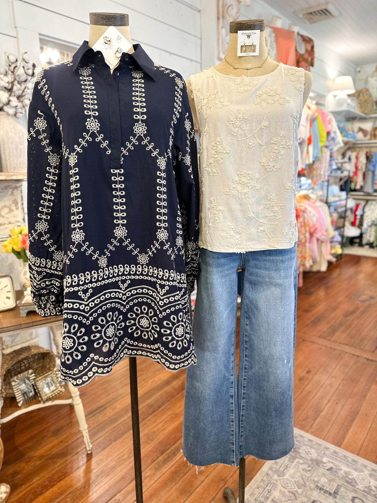 Two mannequins wearing a navy patterned top and beige sleeveless top with blue jeans in a store setting.