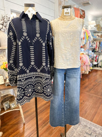 Two mannequins wearing a navy patterned top and beige sleeveless top with blue jeans in a store setting.