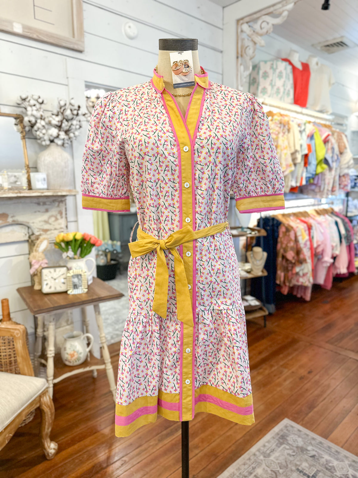Colorful dress on a mannequin in a store setting with floral arrangements and furniture. oh my stars clothing line 