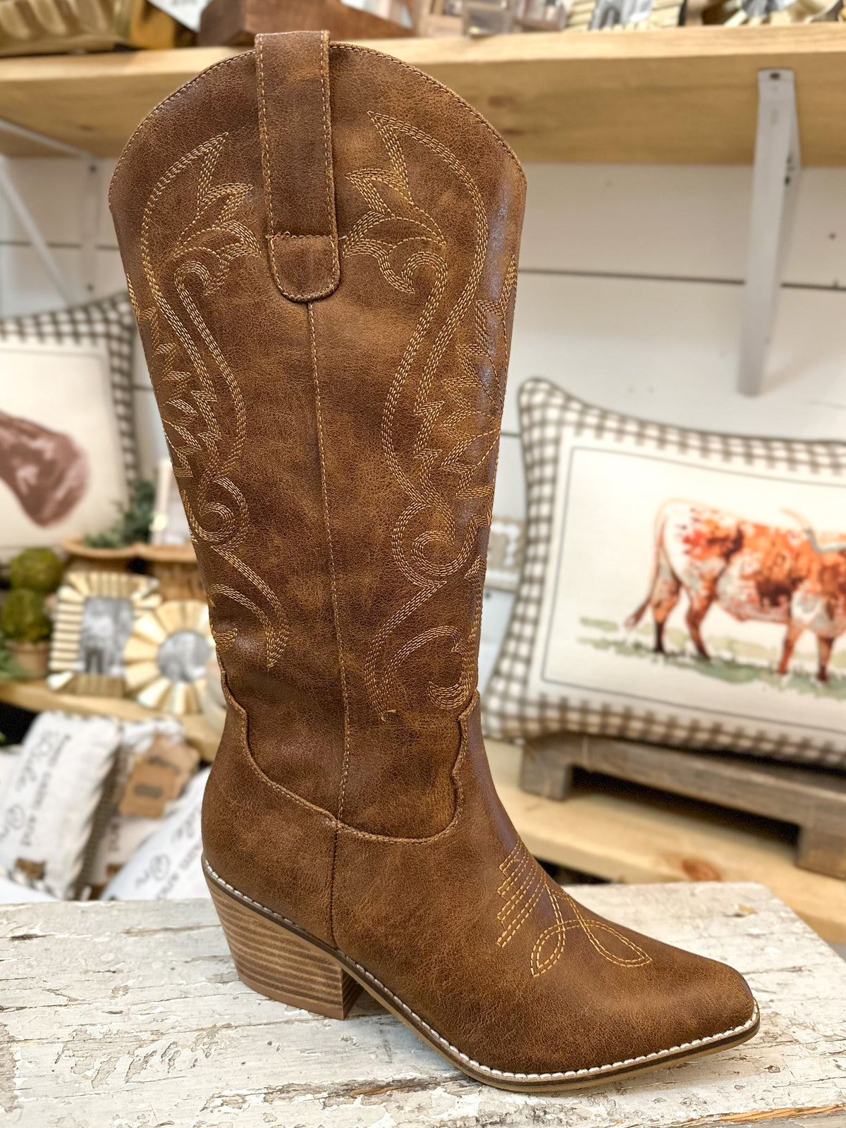 Brown cowboy boot with intricate designs on a wooden surface.