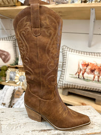 Brown cowboy boot with intricate designs on a wooden surface.