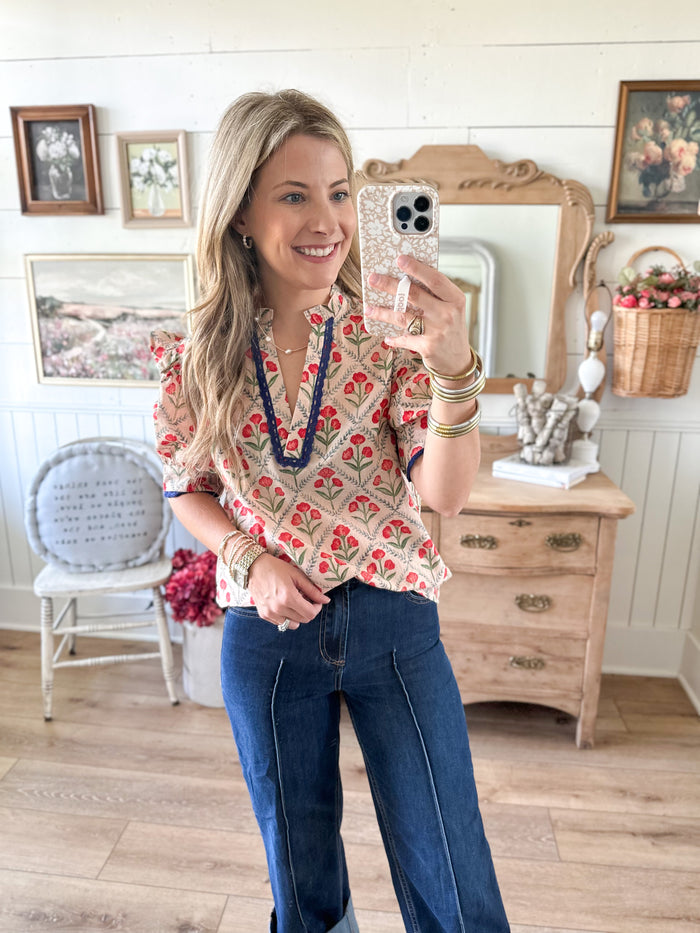 Woman taking a mirror selfie wearing a floral blouse and jeans in a home setting.
