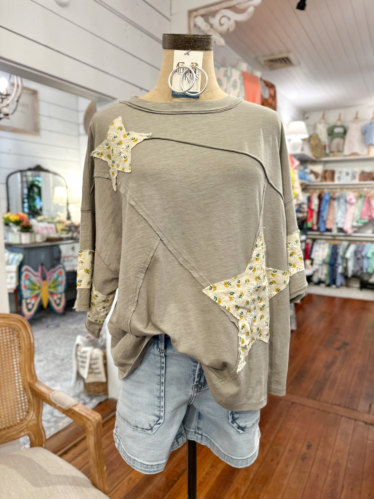 Olive green sweater with star patterns on a mannequin in a store setting.