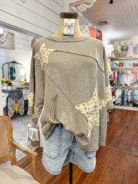 Olive green sweater with star patterns on a mannequin in a store setting.