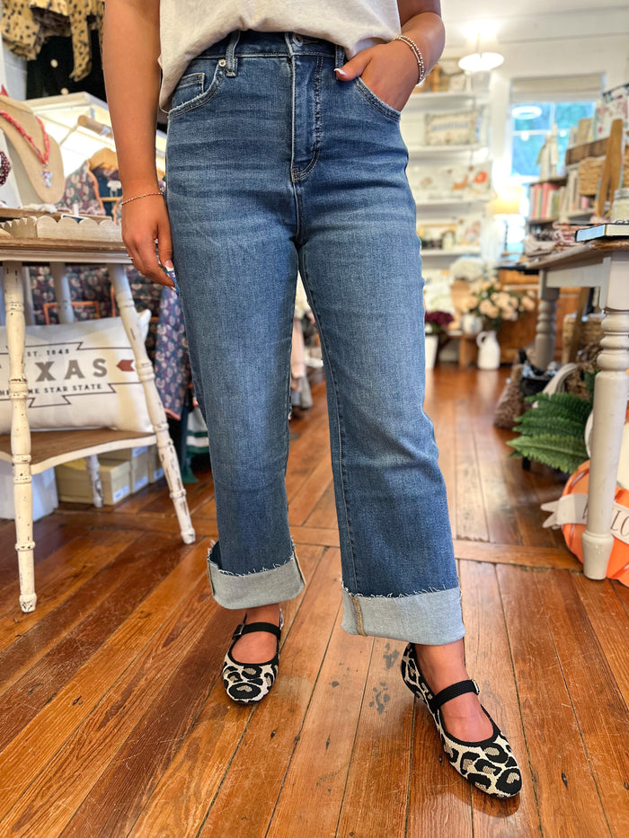Person wearing blue jeans and leopard print shoes on a wooden floor.