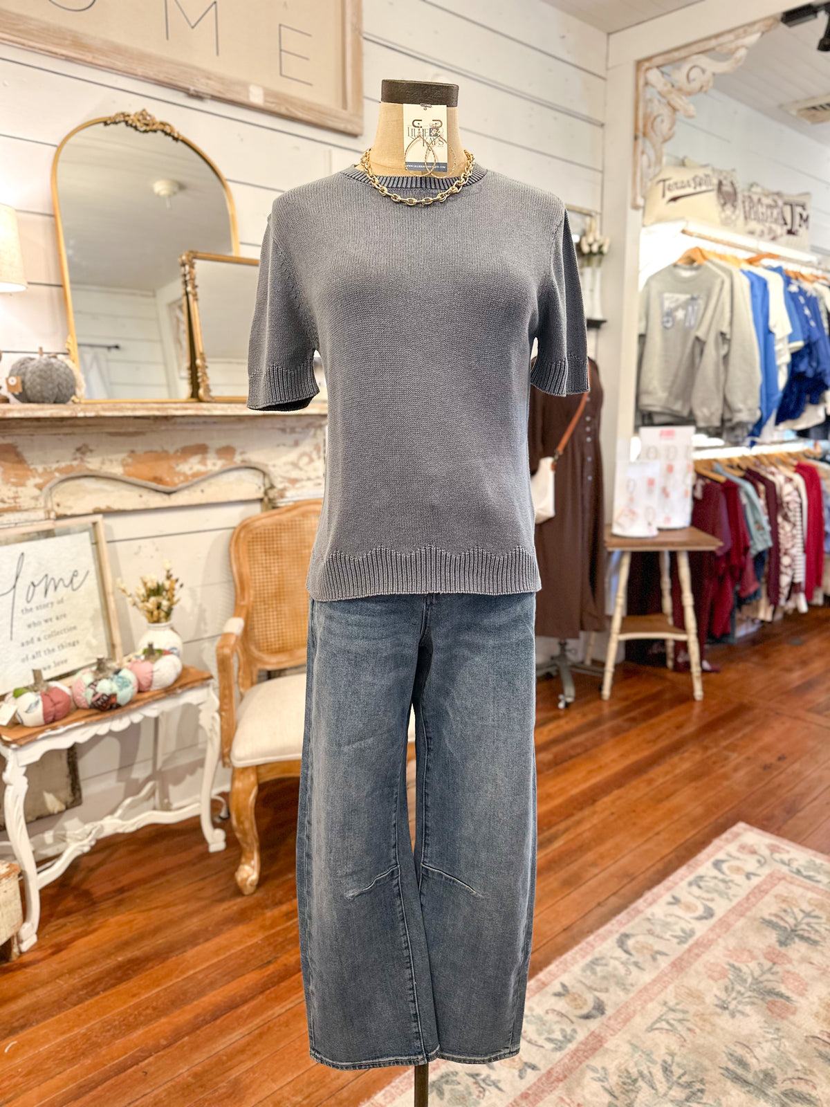 Mannequin wearing a dusty blue sweater and blue jeans in a store setting with mirrors and clothing racks.