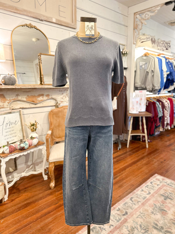 Mannequin wearing a dusty blue sweater and blue jeans in a store setting with mirrors and clothing racks.
