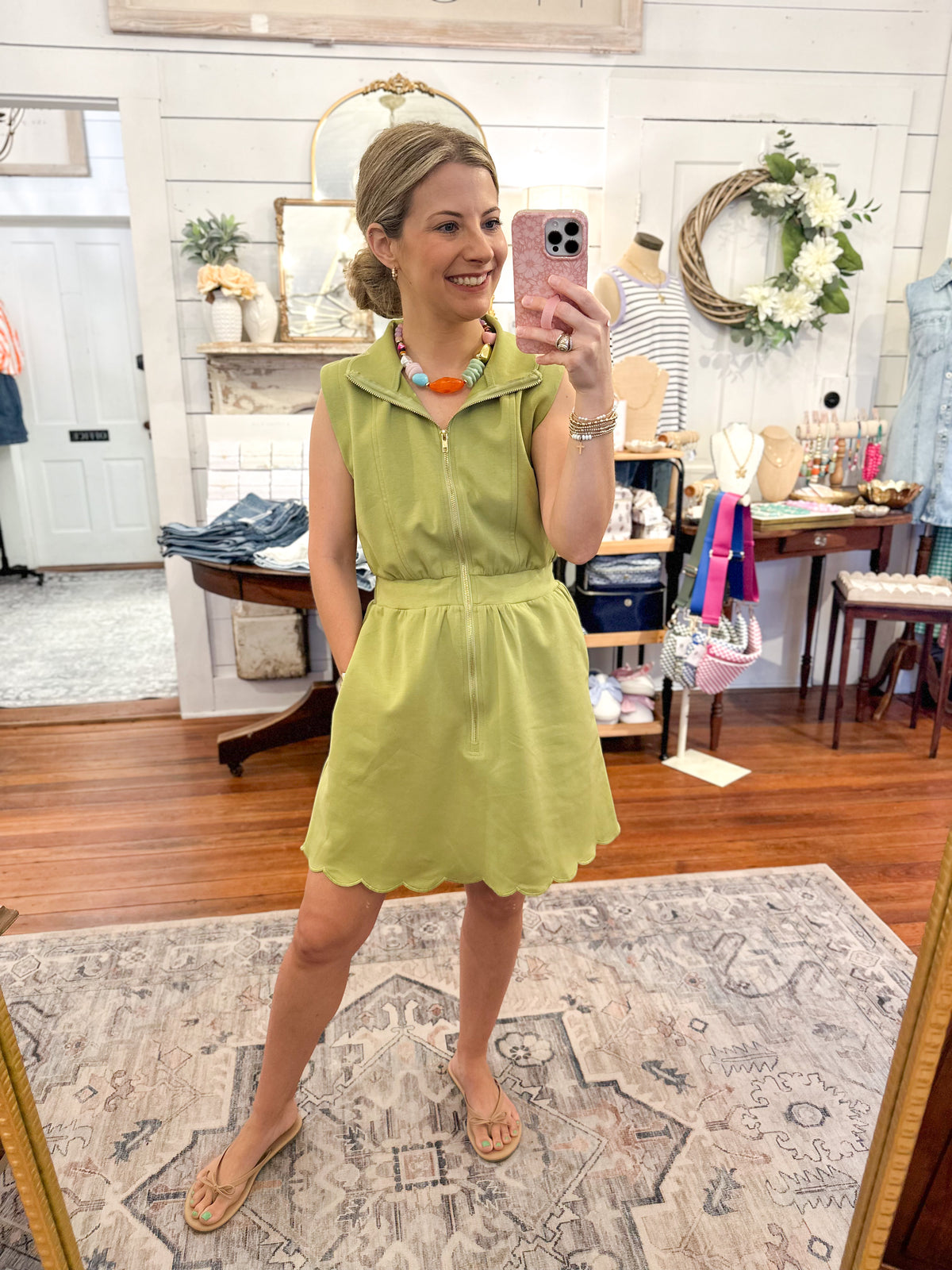Woman taking a mirror selfie wearing a green dress in a store.