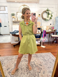 Woman taking a mirror selfie wearing a green dress in a store.