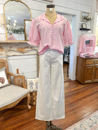 Mannequin wearing a pink checkered blouse and white pants in a room with wooden floor and furniture.
