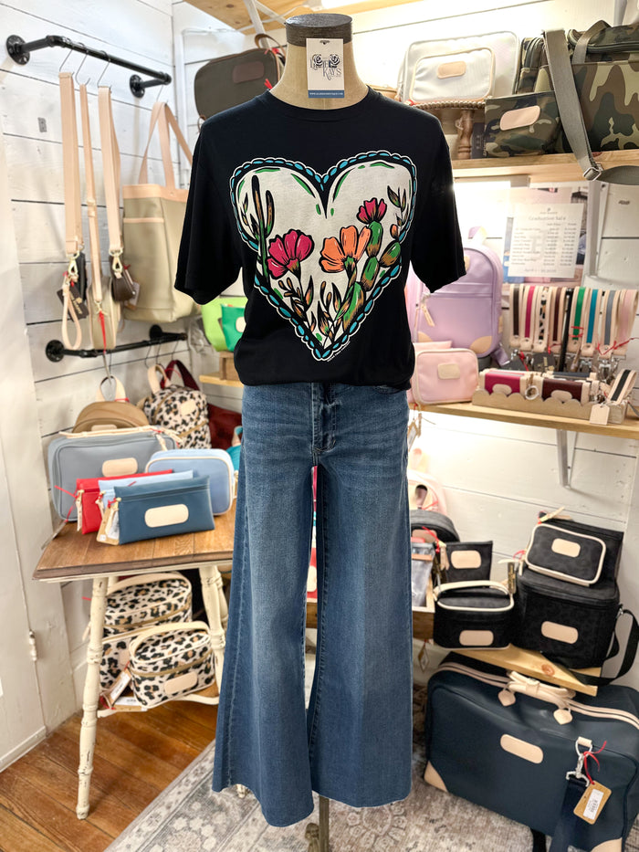 Mannequin wearing a black t-shirt with a colorful heart design and blue jeans in a store setting.