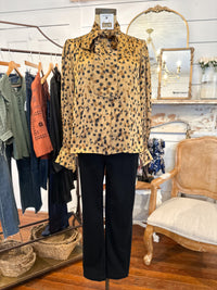 Mannequin wearing a leopard print top and black pants in a store setting with clothing racks and a chair in the background.
