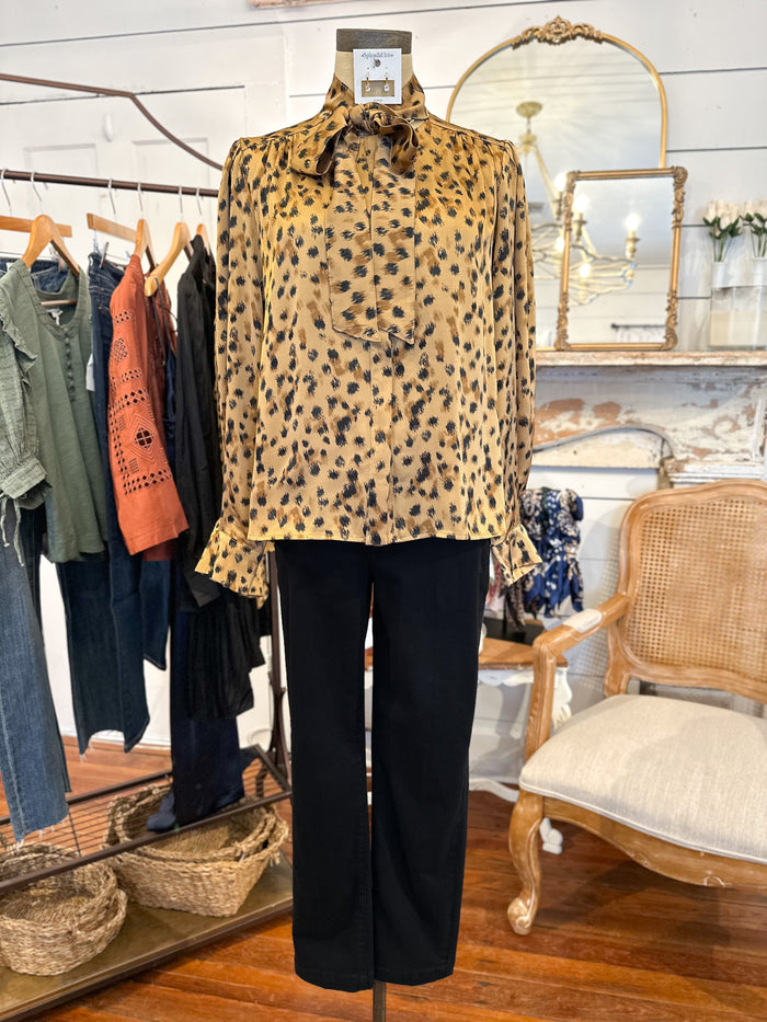 Mannequin wearing a leopard print top and black pants in a store setting with clothing racks and a chair in the background.