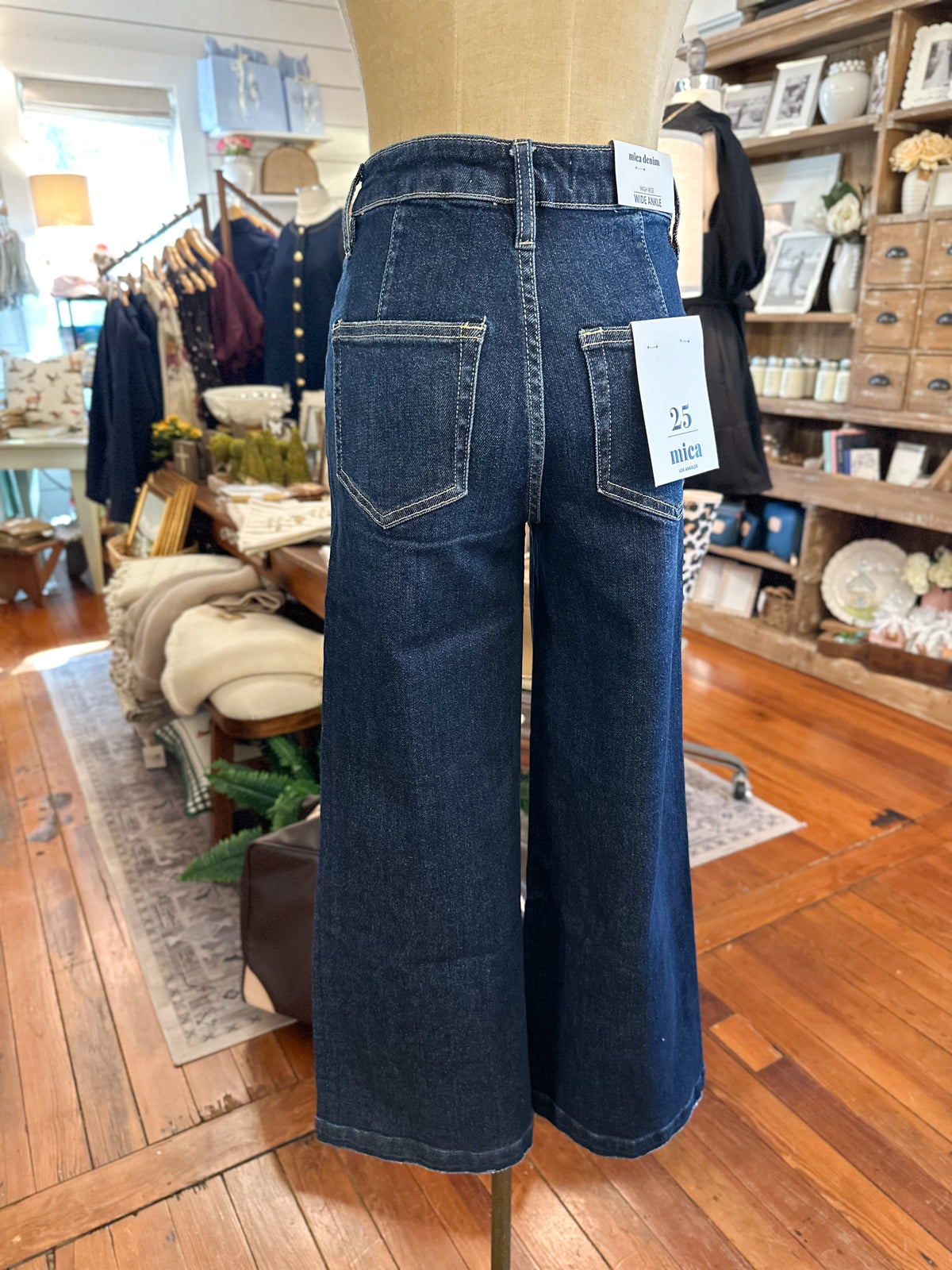 Dark wash blue wide-leg denim jeans displayed on a mannequin in a clothing boutique, with a white size tag reading '25 medium' attached to the back pocket.