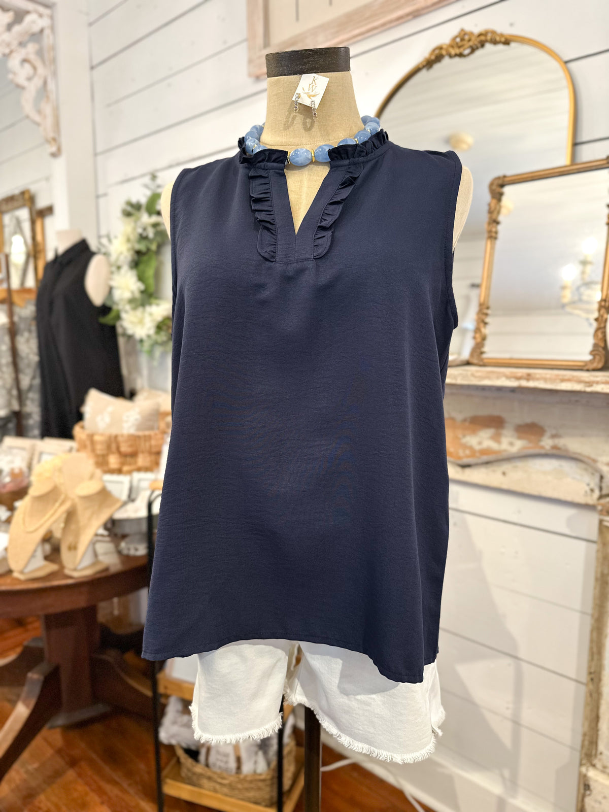 Navy sleeveless top with ruffled neckline on a mannequin in a store setting.