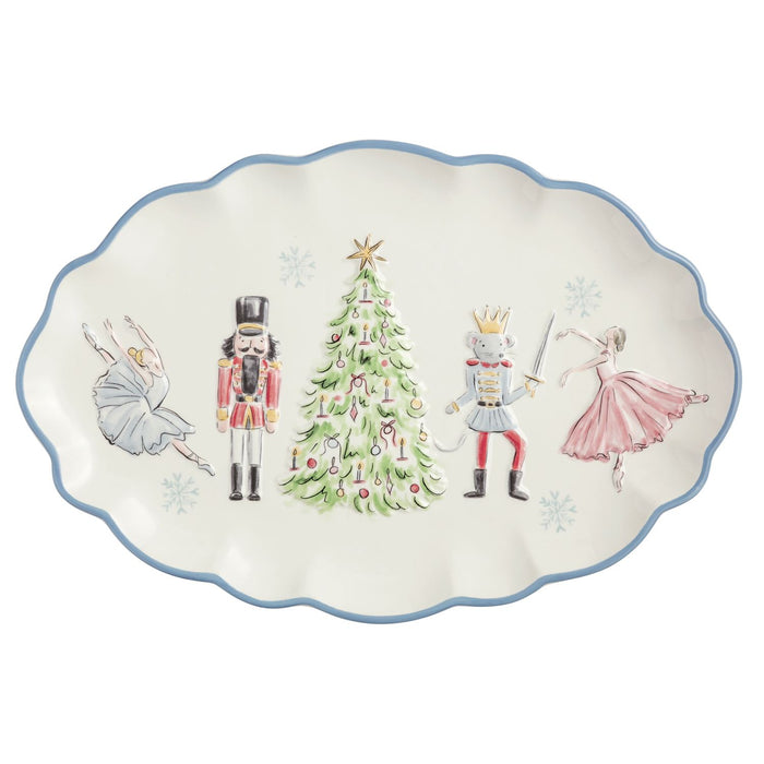 An oval ceramic serving platter with a scalloped edge, featuring a festive holiday illustration of a nutcracker, a princess, a prince, and a ballerina around a decorated Christmas tree on an off-white background with a blue rim. mud pie  nutcracker blue scallop platter 