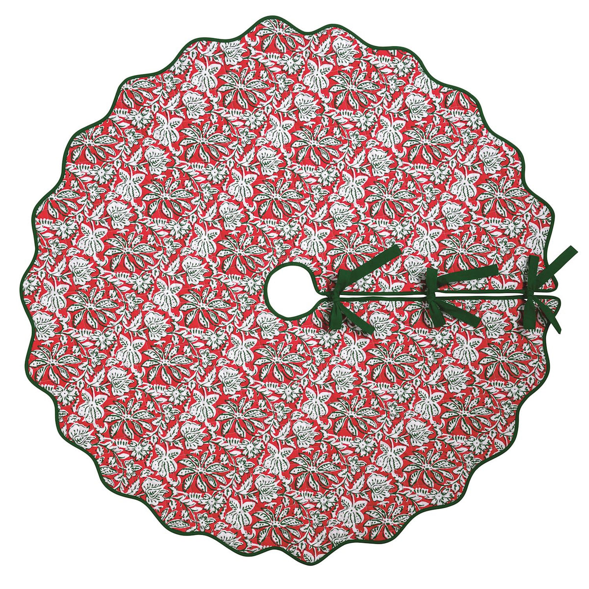 A round Christmas tree skirt with a scalloped edge, featuring a red background with a white and green pine tree and snowflake pattern, finished with dark green ribbon ties.