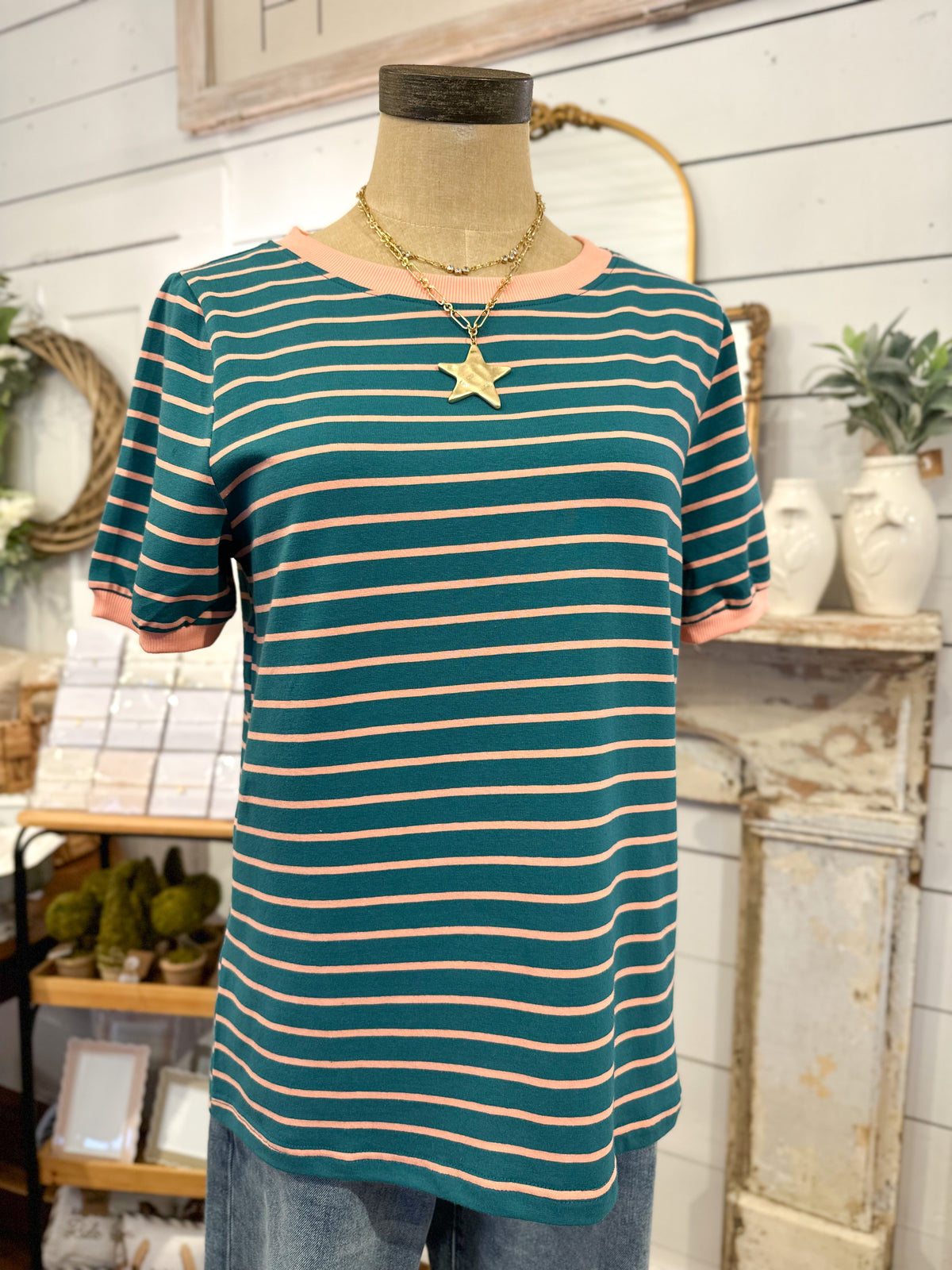Mannequin wearing a green and beige striped shirt with a star necklace in a store setting.