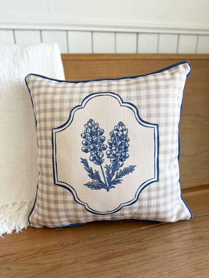 Decorative pillow with blue floral design on a checkered background, placed on a wooden surface.