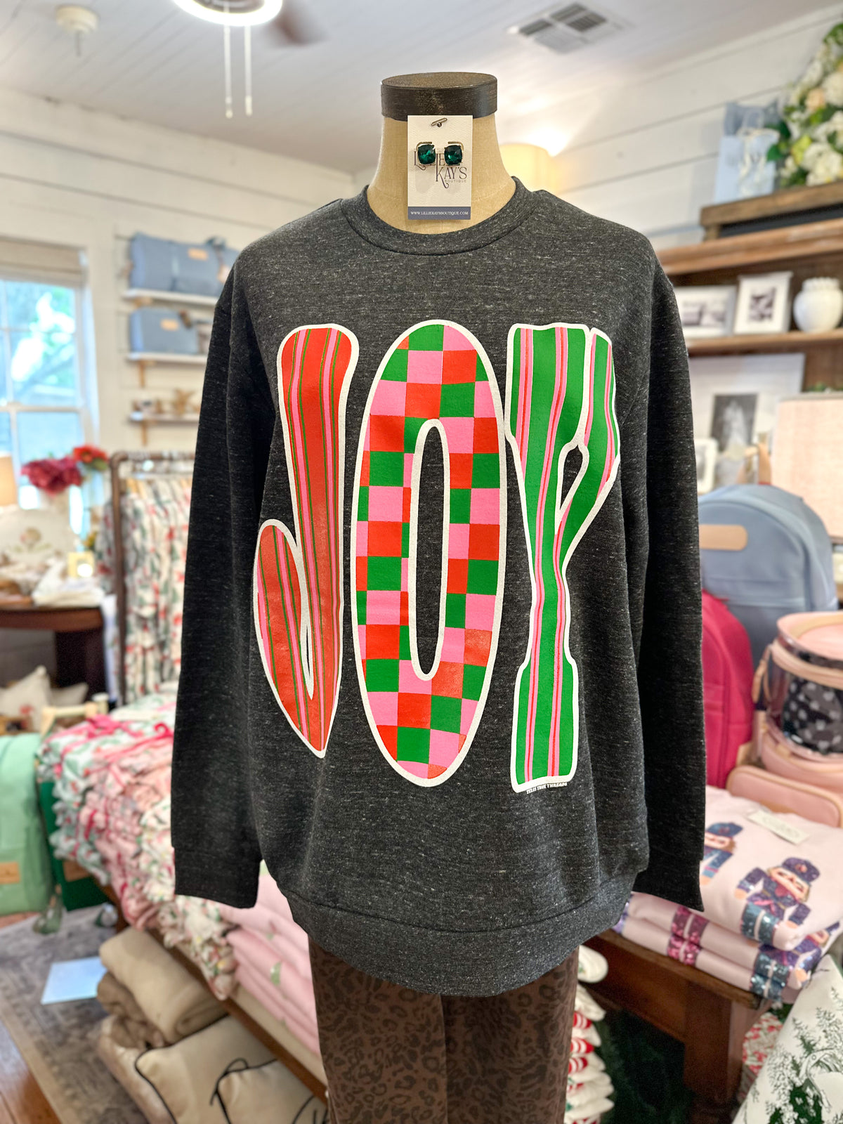 Grey pull over sweater with joy in colorful print and font screen printed on the front inside store setting 