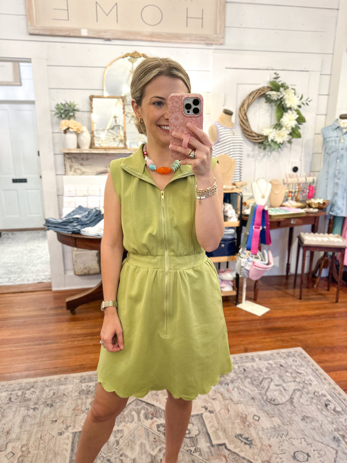 Woman taking a mirror selfie wearing a light green dress in a store setting.