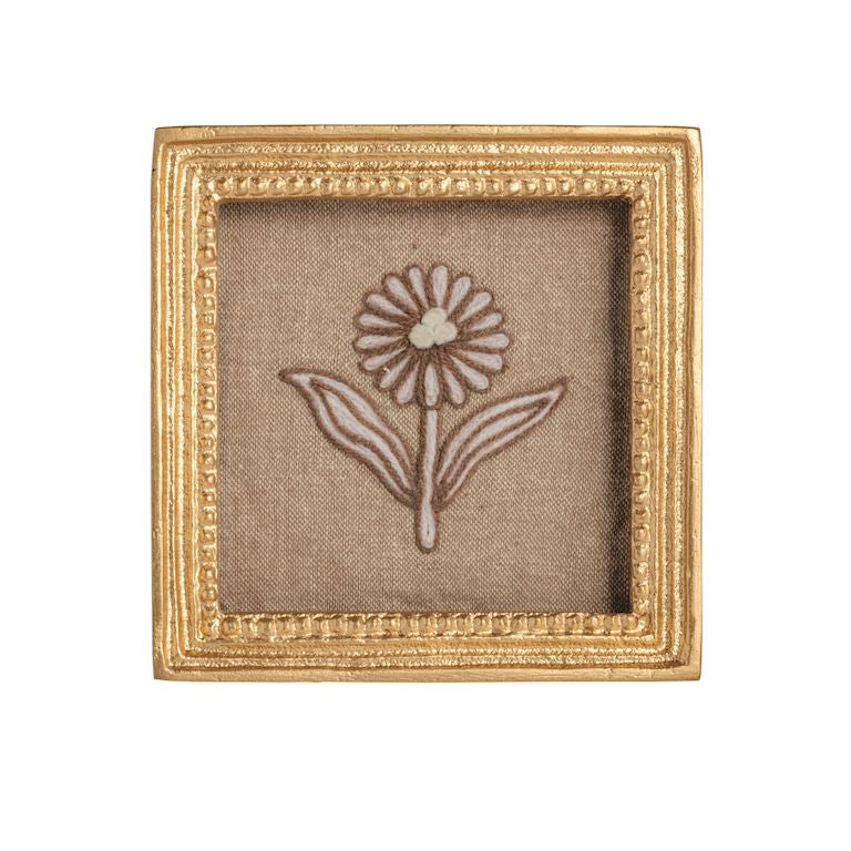 Small embroidered flower on fabric inside a decorative gold frame.