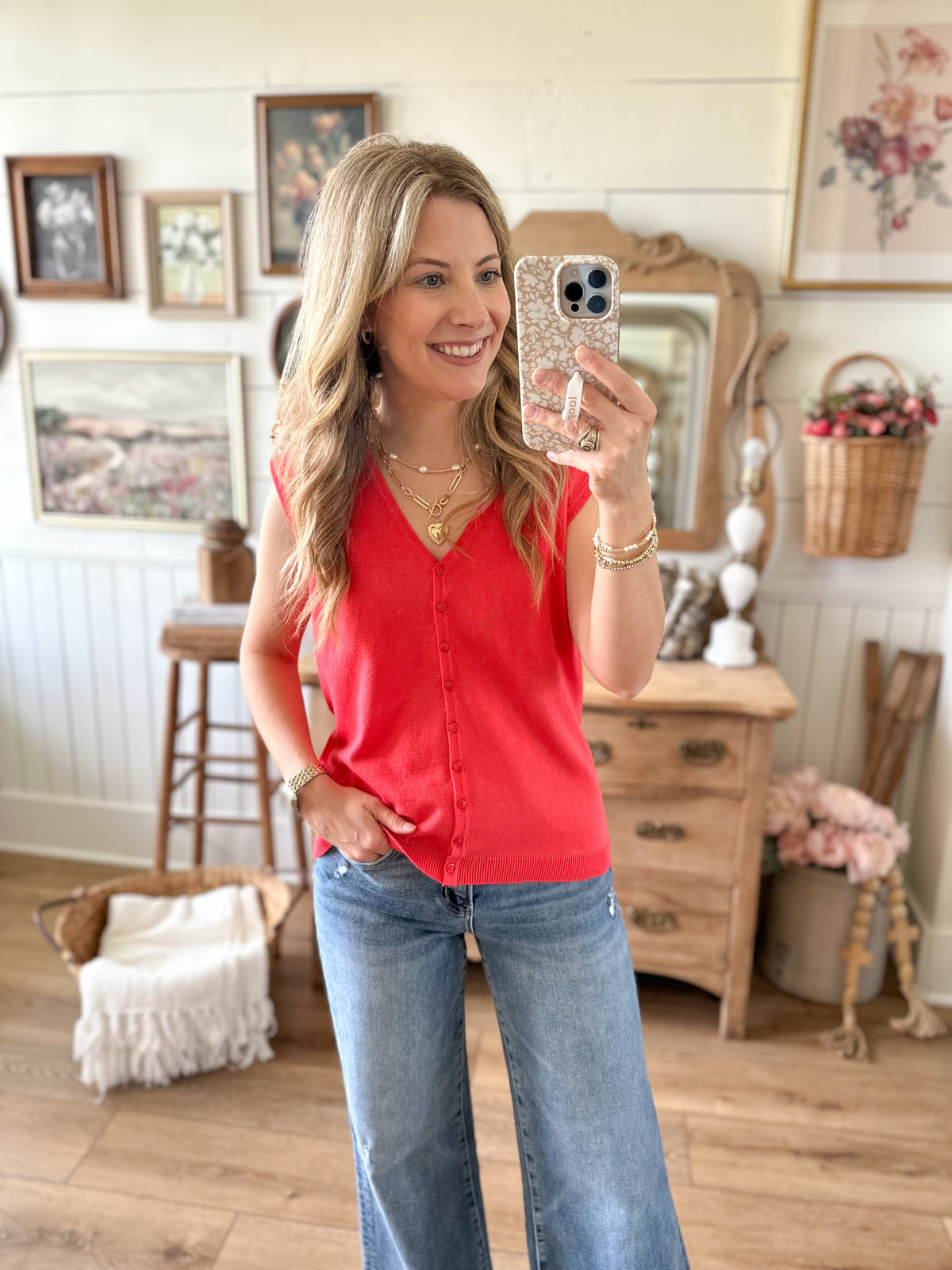 Woman taking a mirror selfie wearing a bright coral top and blue jeans in a home setting.