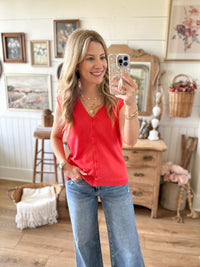 Woman taking a mirror selfie wearing a bright coral top and blue jeans in a home setting.