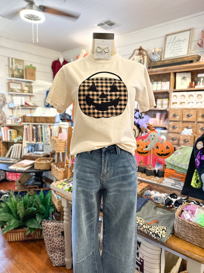 Mannequin wearing a beige t-shirt with a checkered pumpkin design in a store setting.