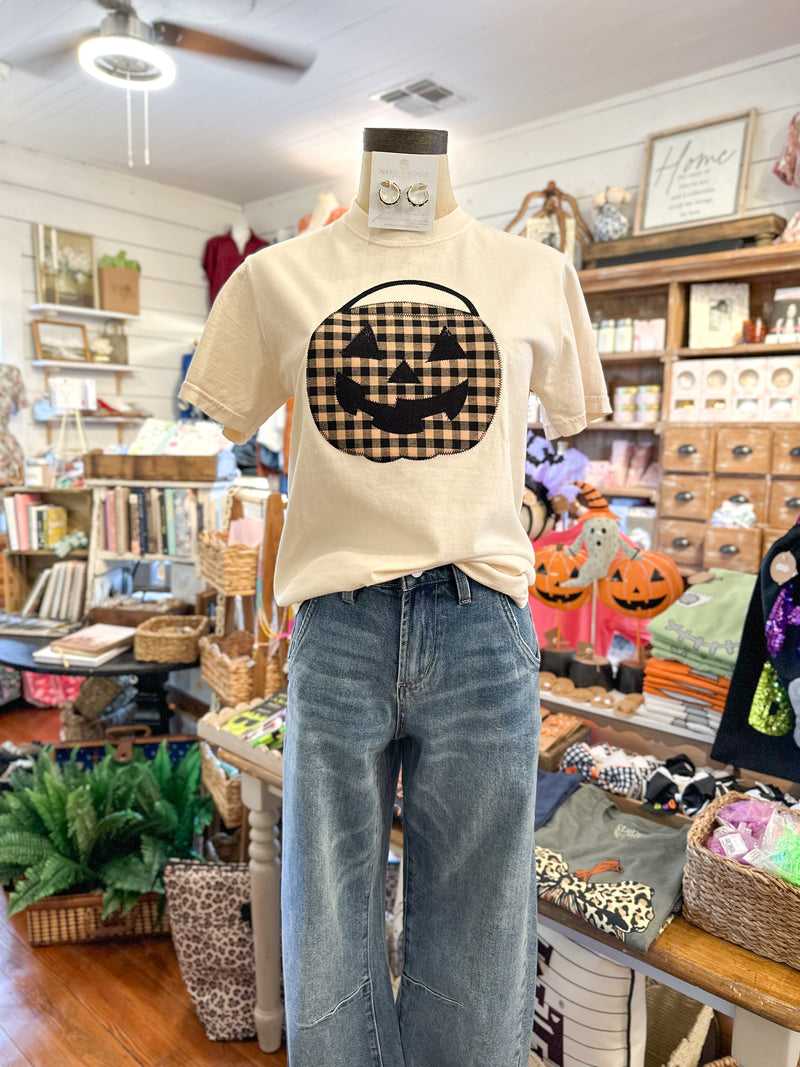 Mannequin wearing a beige t-shirt with a checkered pumpkin design in a store setting.