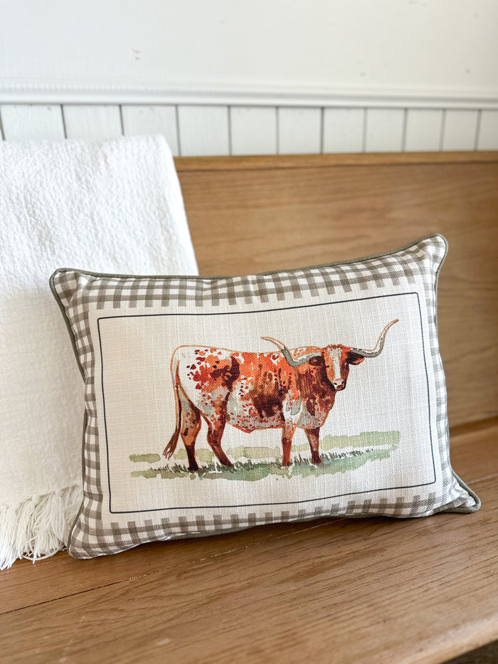 Decorative pillow with a longhorn bull design on a checkered background, placed on a wooden surface.