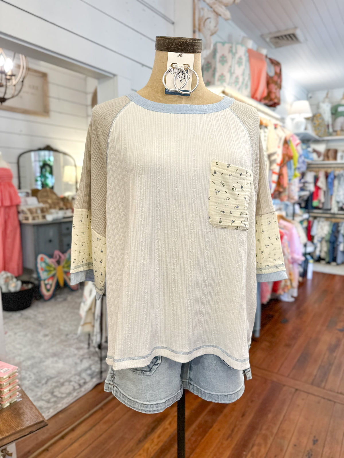 Mannequin wearing a cream-colored long-sleeve top with floral details in a store setting.