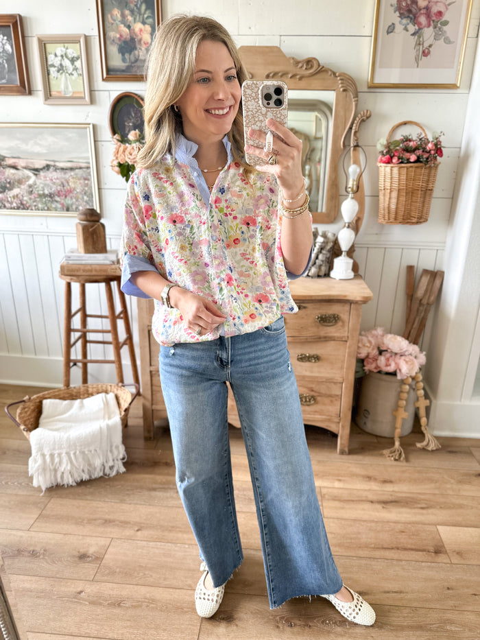 Woman taking a mirror selfie in a floral shirt and jeans in a home setting.