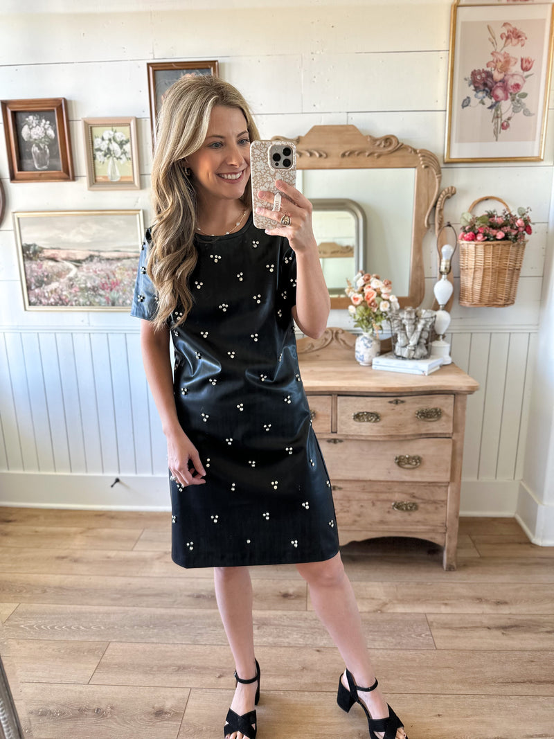 Woman taking a mirror selfie wearing a black dress with white polka dots in a home setting.