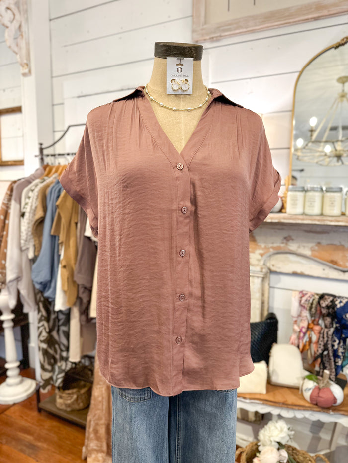 mauve color button-up shirt on a mannequin in a store setting with clothing racks and decor in the background.